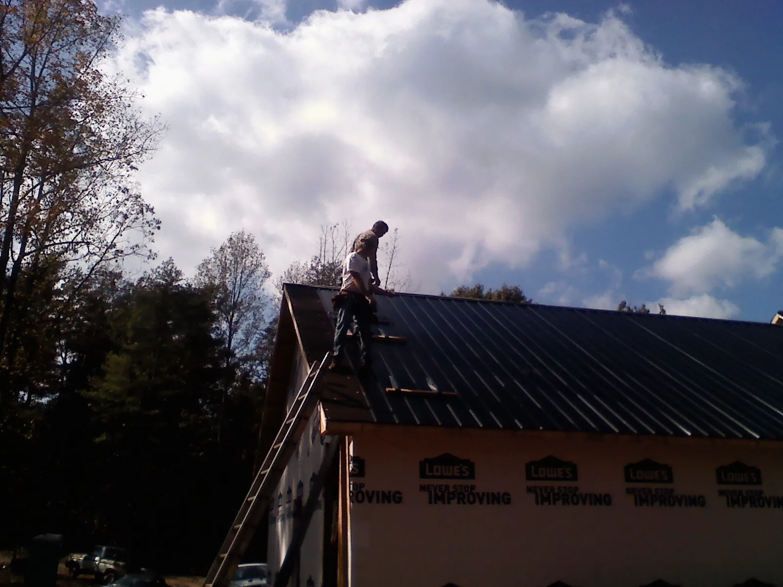 Roofer fastening dark metal panels high against a cloudy sky, from a Roof Inspection job in Littleton